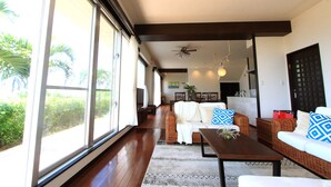 A spacious living area with large windows, a ceiling fan, and a kitchen in the background. - Ryukyu Ritei Ingya (Miyakojima)