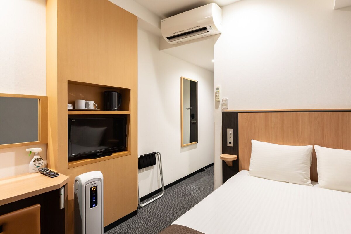 A hotel room with a bed, a desk with a coffee maker, a TV, a microwave, and a bathroom with a mirror and sink.