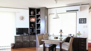 A dining area with a glass table and wicker chairs, a dark wooden cabinet with drawers, a television, and a decorative wall piece. - Pontoon <ishigakijima> (Ishigaki)