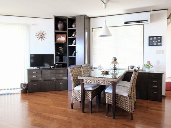 A dining area with a glass table and wicker chairs, a dark wooden cabinet with drawers, a television, and a decorative wall piece. - Pontoon <ishigakijima> (Ishigaki)