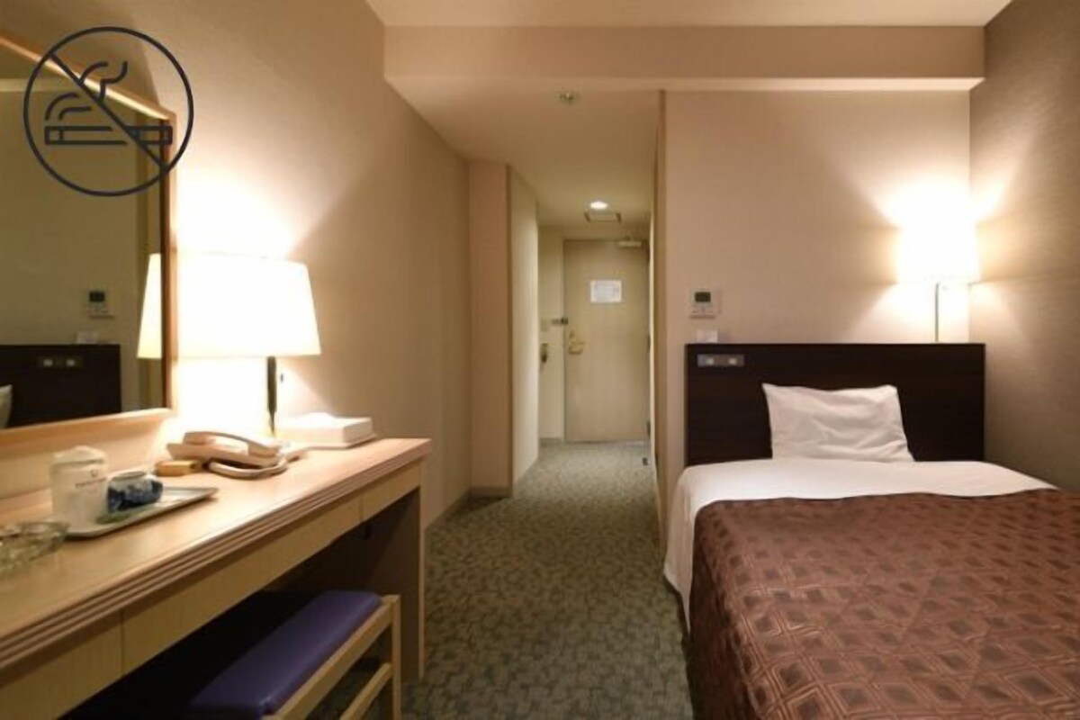 Une chambre d’hôtel comprenant un lit, une lampe de chevet, un bureau avec une lampe et un miroir.