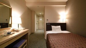 Une chambre d’hôtel avec un lit, un bureau doté d’une lampe, un miroir et une salle de bain visible à travers une porte.