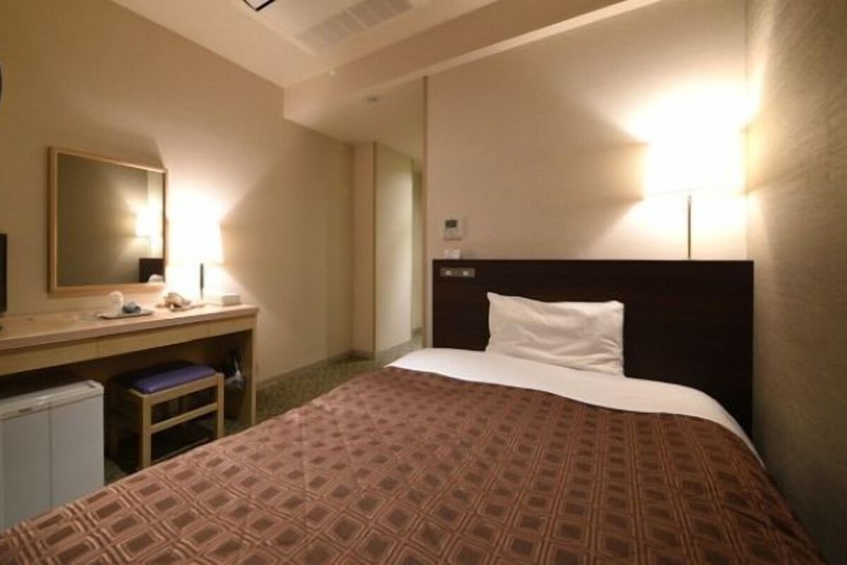 Une chambre d’hôtel comprenant un lit, un bureau avec une chaise, une télévision et un miroir.