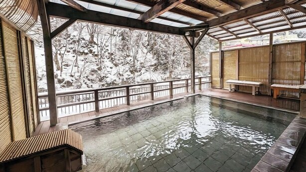 A covered outdoor pool with a wooden deck, benches, and a view of a snowy landscape. - Kawaji Onsen Ichiryukaku (Nikko)