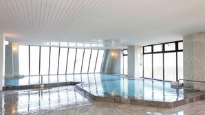 A large indoor swimming pool with clear glass walls, a tiled floor, and a high ceiling with a grid pattern. - Kawaji Onsen Ichiryukaku (Nikko)