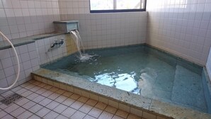 Eine kleine, rechteckige Whirlwanne mit einem Wasserhahn, geflieste Wände und einem Fenster darüber.
