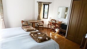 Ein Hotelzimmer mit zwei Betten, einem Esstisch, Stühlen, einem Schreibtisch mit Computer, einem Spiegel und einem Kleiderschrank.