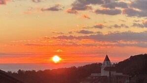 Ein Sonnenuntergang über einer Küstenlandschaft mit einem markanten Gebäude mit spitzer Dachform.