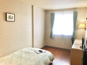 A bedroom with a bed, a desk, a lamp, and a window with curtains.