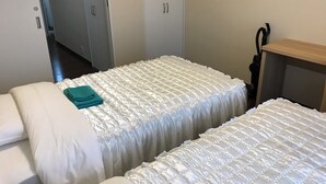 A hotel room with two beds, each with white bedding and teal towels. There is a wooden nightstand and a door with a handle.