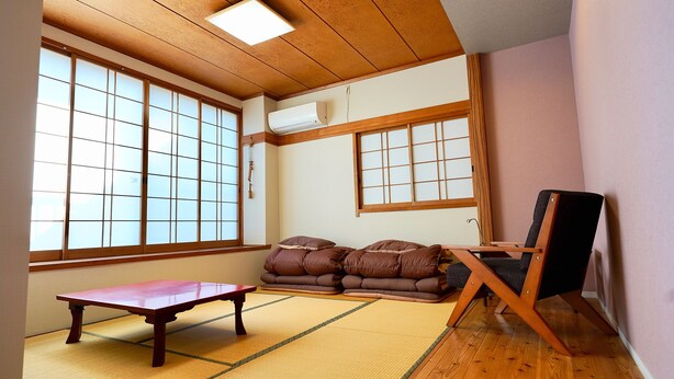 Een traditionele Japanse kamer met tatami vloerbedekking, een lage houten tafel, kussens en een futonbed.