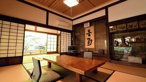 Une pièce de style japonais traditionnel, avec un sol recouvert de tatamis, une table en bois, un siège en tatami, un téléviseur et une porte coulissante donnant sur un jardin.