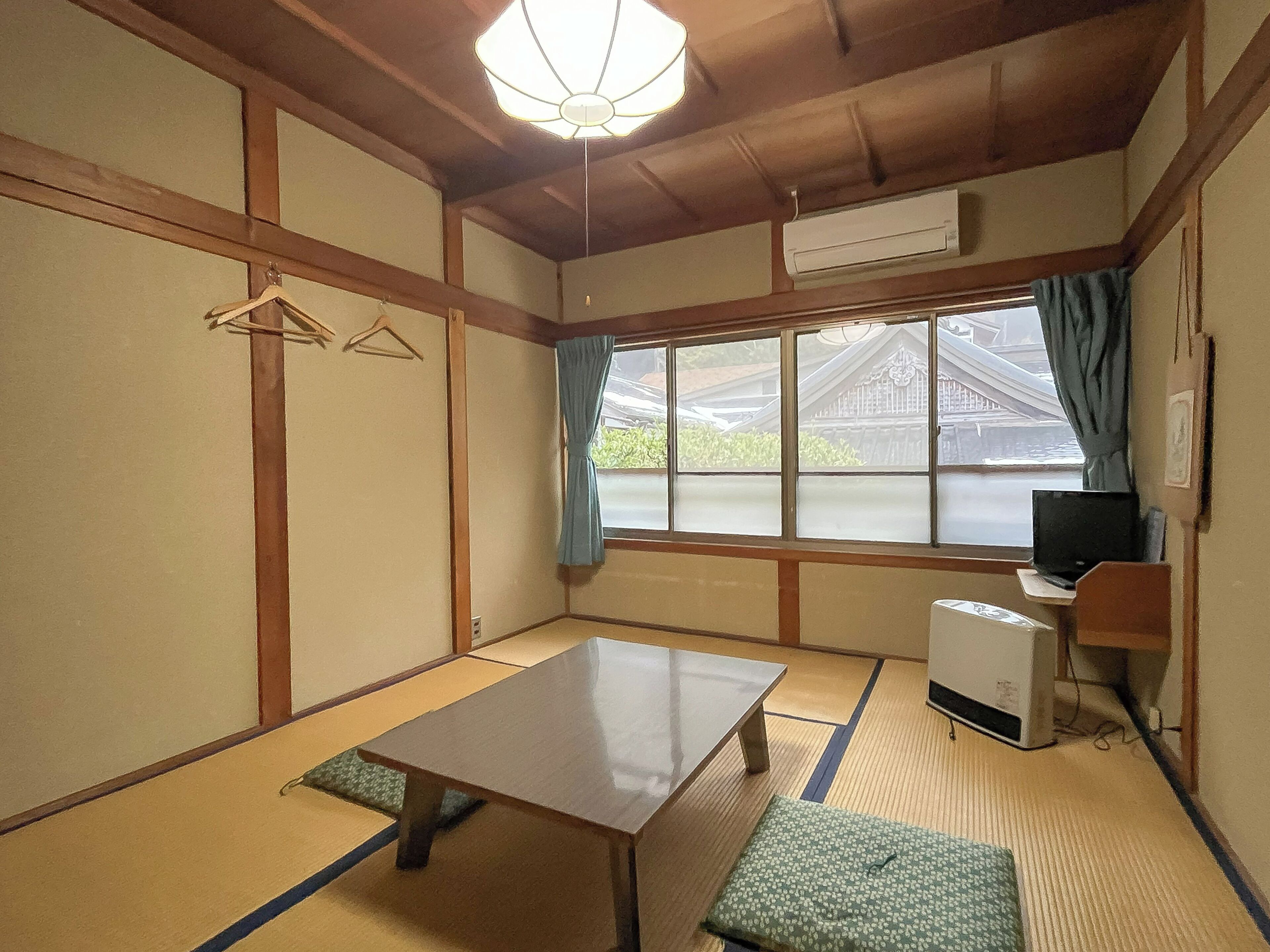 Una habitación japonesa tradicional con suelo de tatami, una mesa baja, un banco, un escritorio con una computadora y vistas a un edificio tradicional exterior.