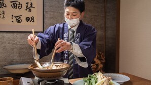 A person in a traditional Japanese outfit preparing a bowl of ramen with chopsticks. - Tanba Sasayama Kinmata (Sasayama)