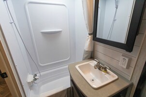 Un baño pequeño con una bañera blanca, un lavamanos con grifo y un espejo sobre el lavamanos.