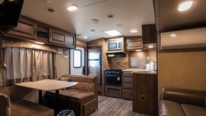 A compact RV kitchen with a microwave, stove, and sink. There is a dining area with a table and benches. - The Trailerhouse Village Yobuko Seaside (Karatsu)
