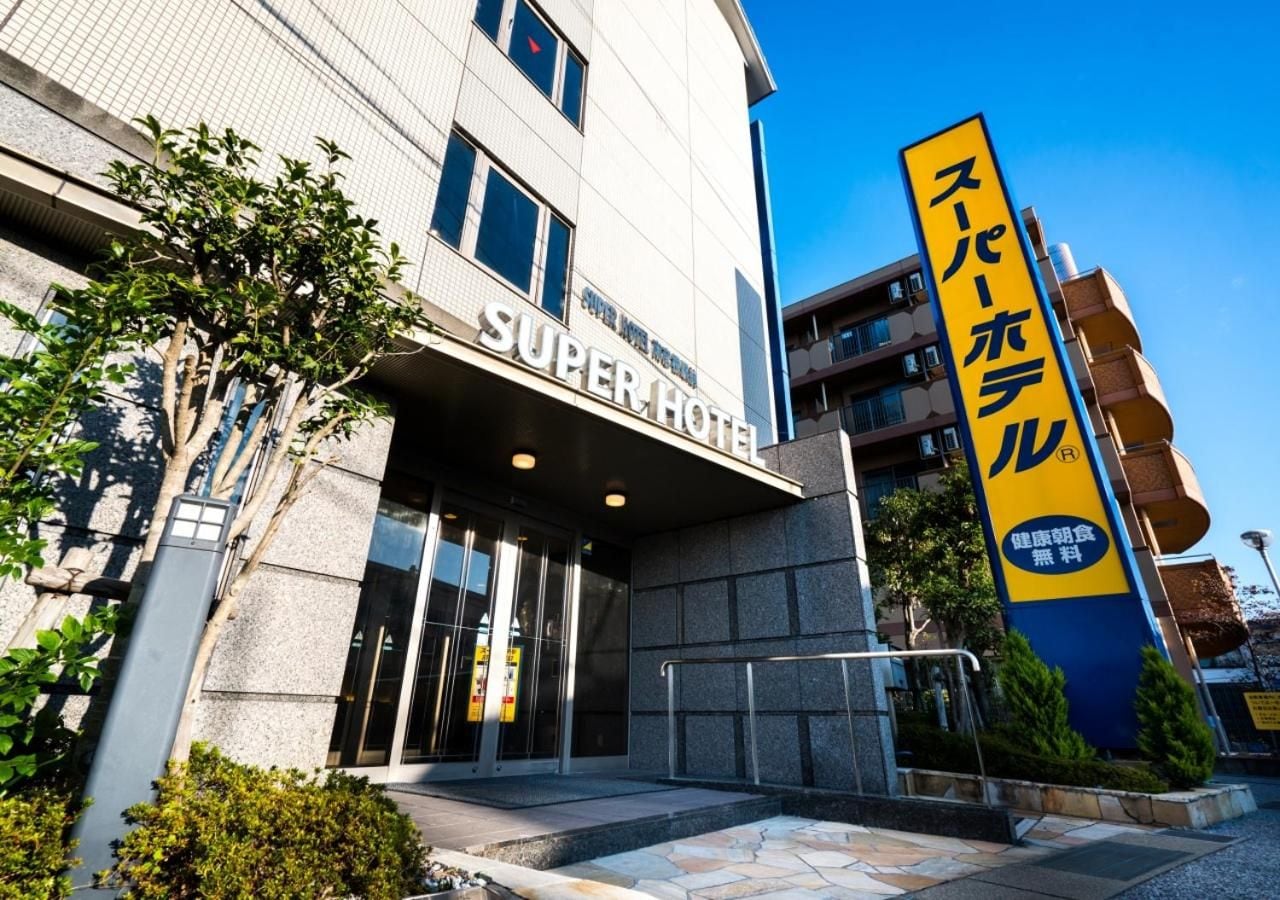 Entrada de un hotel con un cartel que dice 'SUPER HOTEL' y un letrero vertical con caracteres japoneses.