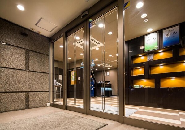 Zona de recepción de hotel con puertas de vidrio, mostrador de recepción y un área de registro.