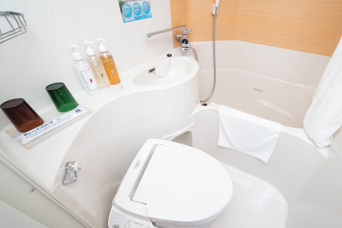 Un baño con lavamanos, inodoro y bañera blancos. Hay artículos de aseo en la encimera del lavamanos.