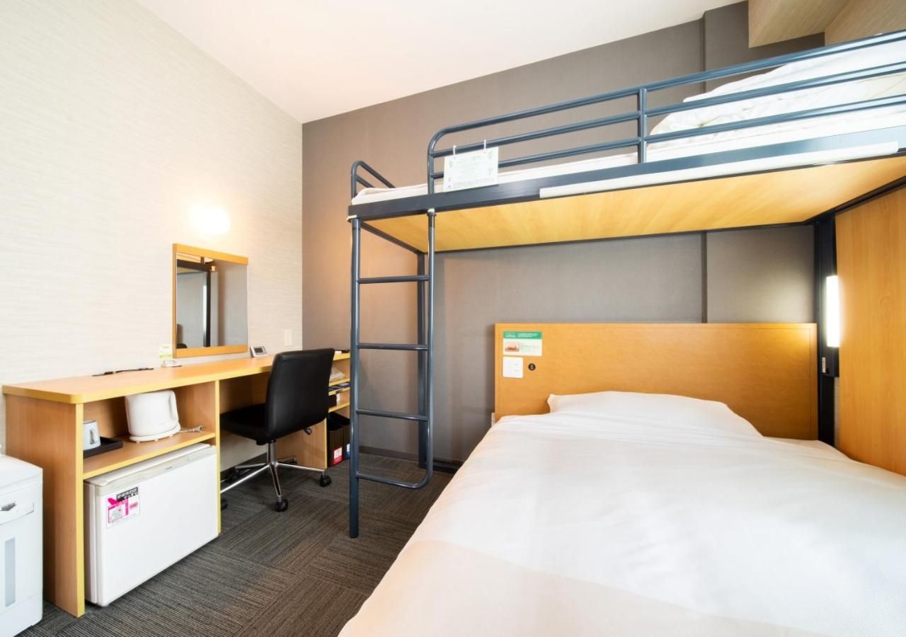 Habitación de hotel con literas, un escritorio con silla, un refrigerador pequeño y un espejo.