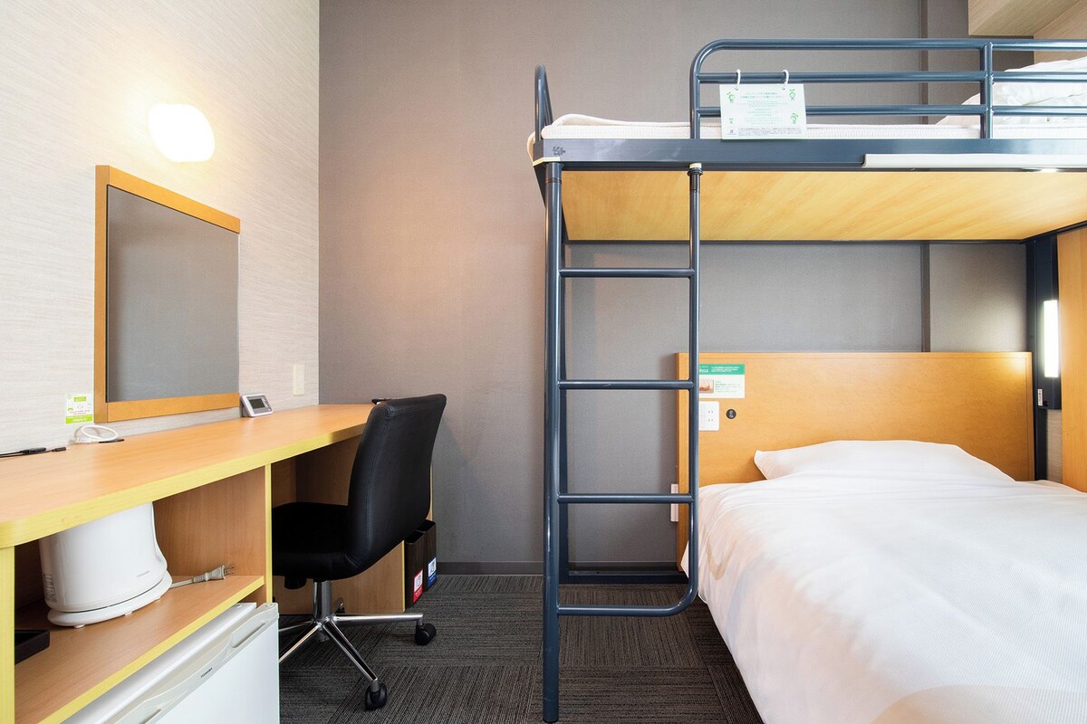 Une chambre avec un lit superposé, un bureau et une chaise, un miroir et une table de chevet.