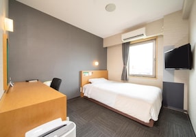 Quarto de hotel com cama, escrivaninha, cadeira, televisão e ar condicionado.