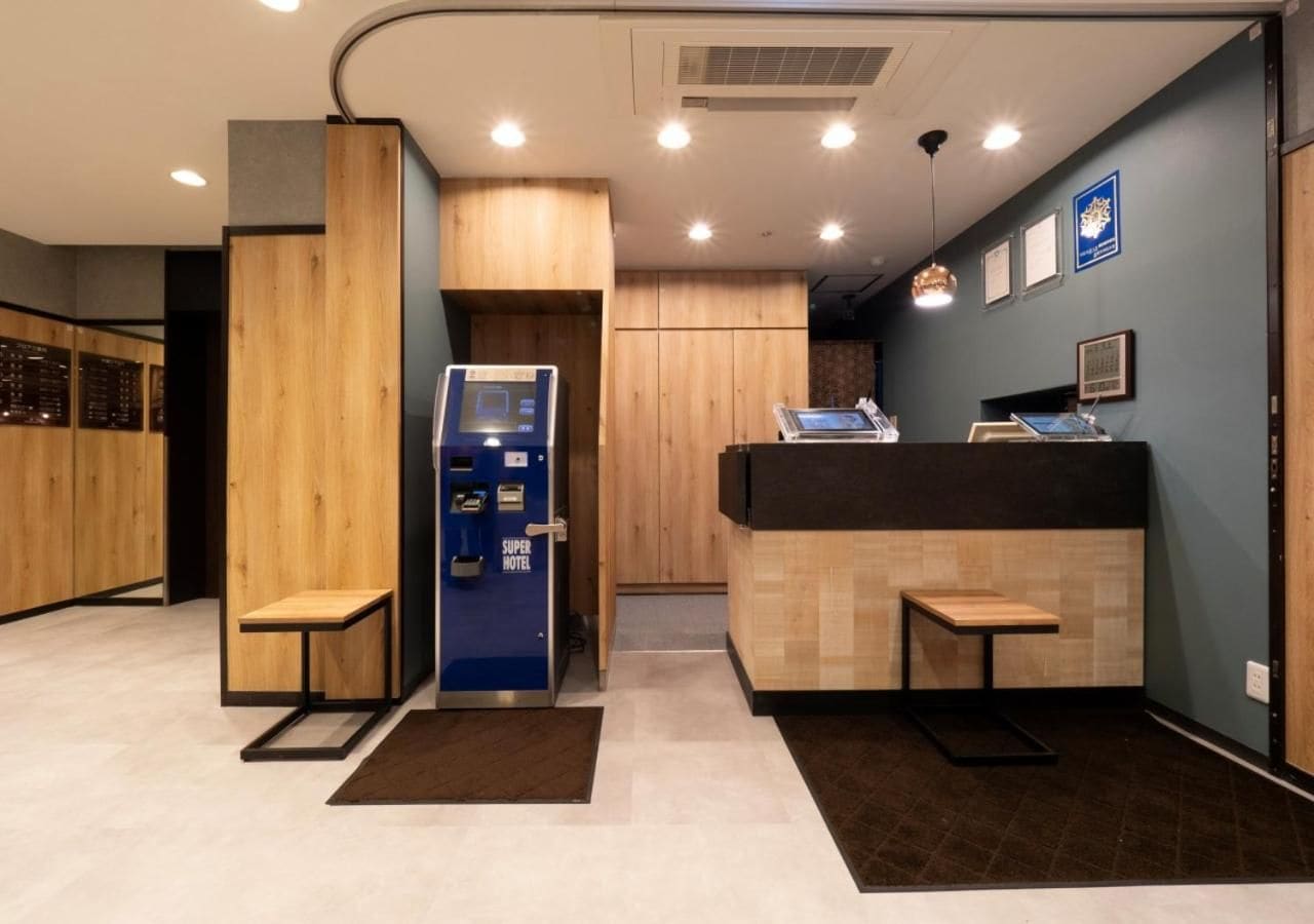 Una zona de recepción con un mostrador de madera, un quiosco de información azul y un banco.