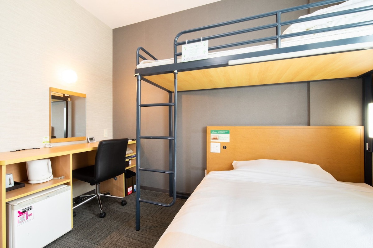 Une chambre avec un lit superposé, un bureau, une chaise et un petit réfrigérateur.