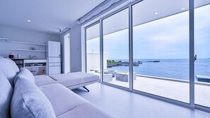 Un salón moderno con un amplio ventanal corredera que da a un balcón con vistas al mar.