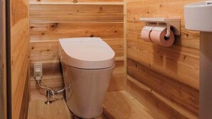 A small, wooden-paneled bathroom with a toilet, a toilet paper holder, and a visible electrical outlet. - Kasamatsutei (Aridagawa)
