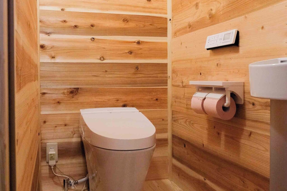 A small, wooden-paneled bathroom with a toilet, a toilet paper holder, and a sink.