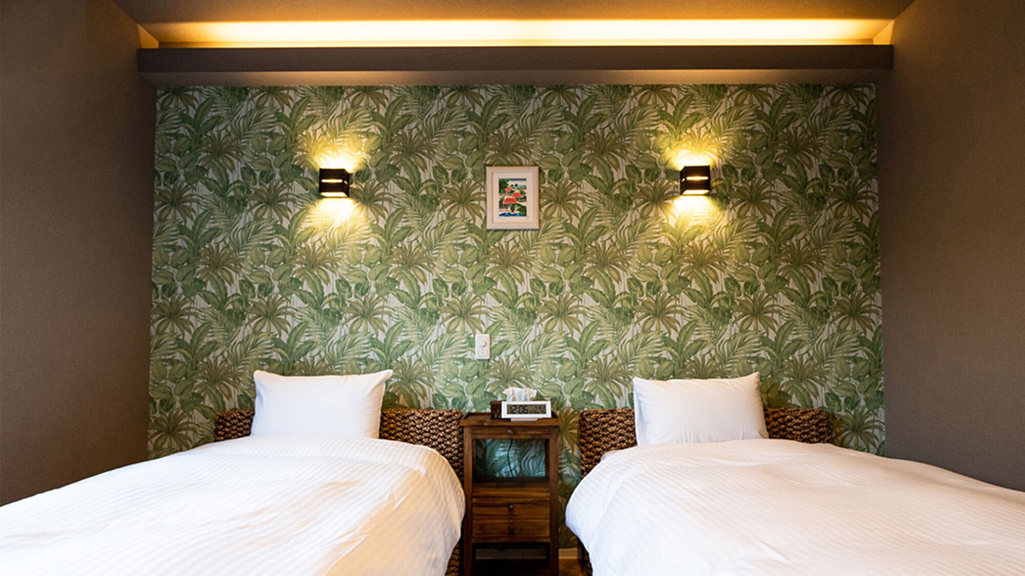 A hotel room with two beds, a nightstand, and a wall with a tropical leaf pattern.