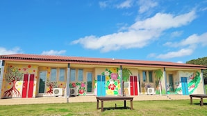 A building with colorful murals, a red roof, and a grassy area in front. - Alezed Villa Shiraho <ishigakijima> (Ishigaki)