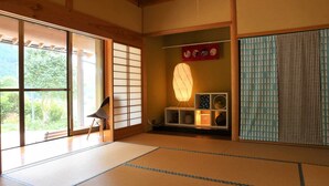 A traditional Japanese room with tatami flooring, a shoji screen, a tatami mat chair, a shelf with decorative items, and a hanging lantern. - Farm Resort Awanowa (Mimasaka)