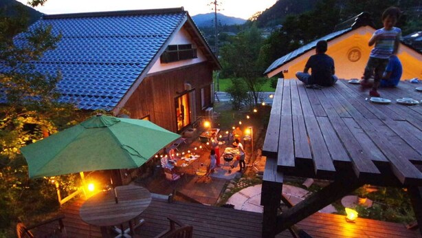 A wooden deck with a table and chairs, a green umbrella, and a barbecue grill. - Farm Resort Awanowa (Mimasaka)