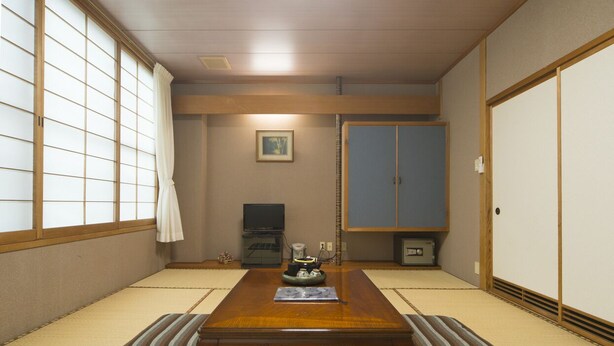 A traditional Japanese room with tatami flooring, a wooden table, a television, and sliding doors. - Shirahamaso (Fukui)