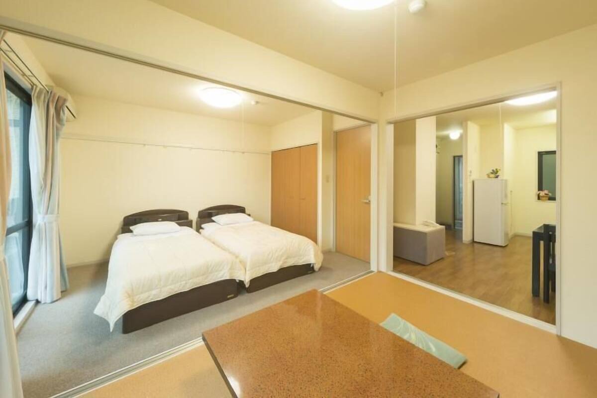 A hotel room with two single beds, a small table, a mirror, and a wardrobe.
