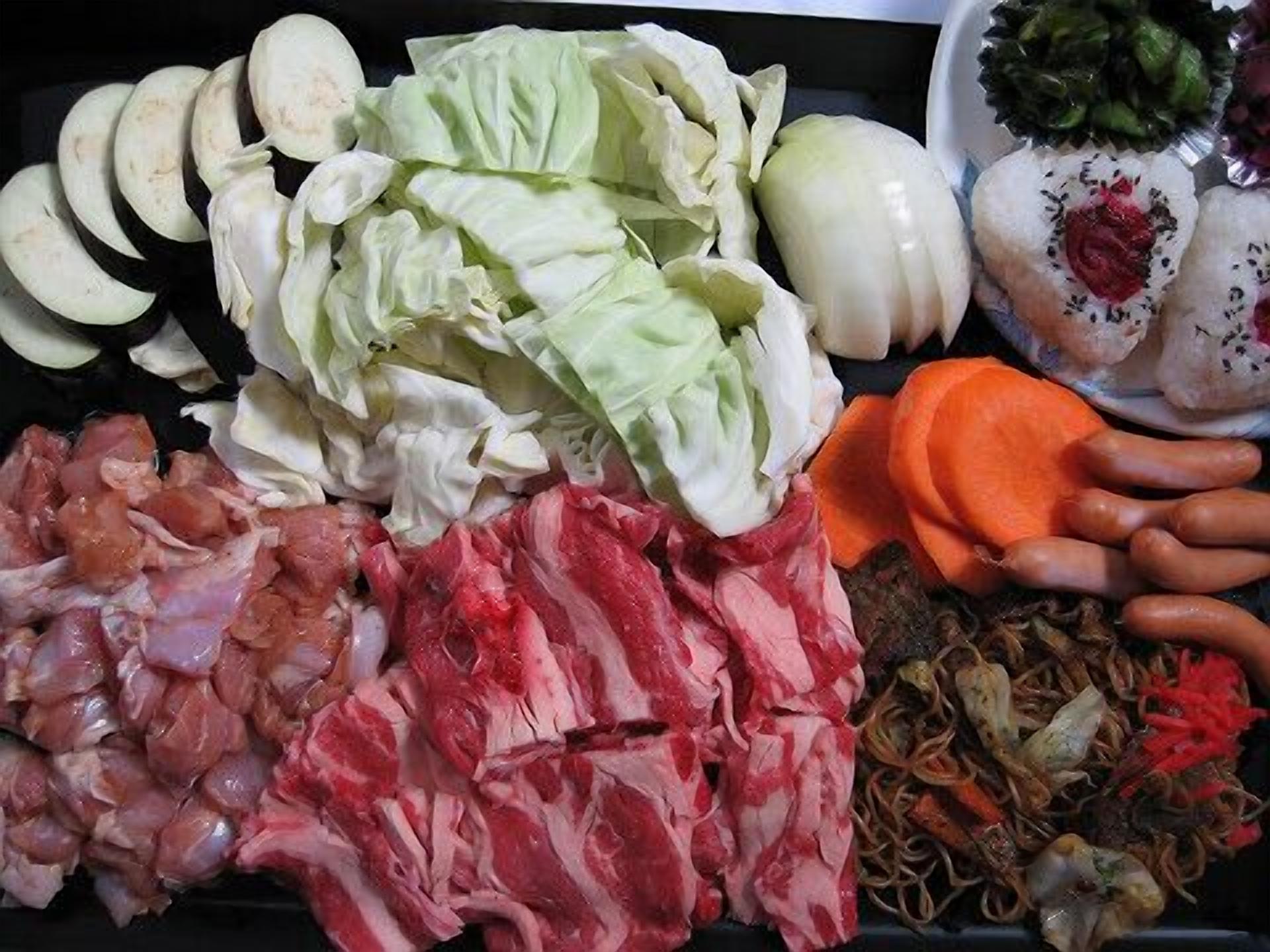 A variety of raw meats, vegetables, and a plate of sushi.