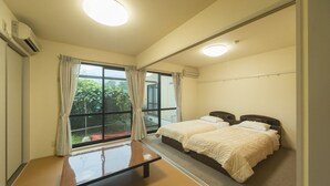 A hotel room with two beds, a large window with curtains, a bedside table, and a mirror. - Shirahamaso (Fukui)