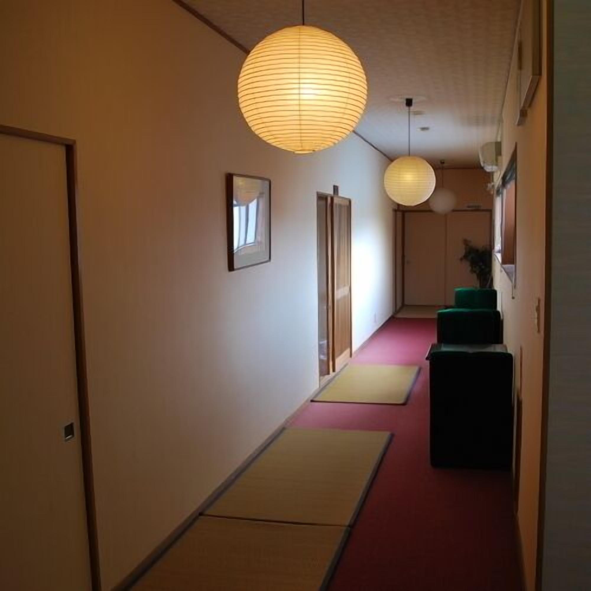 Un couloir avec des tatamis, des portes coulissantes et des lanternes en papier traditionnelles.