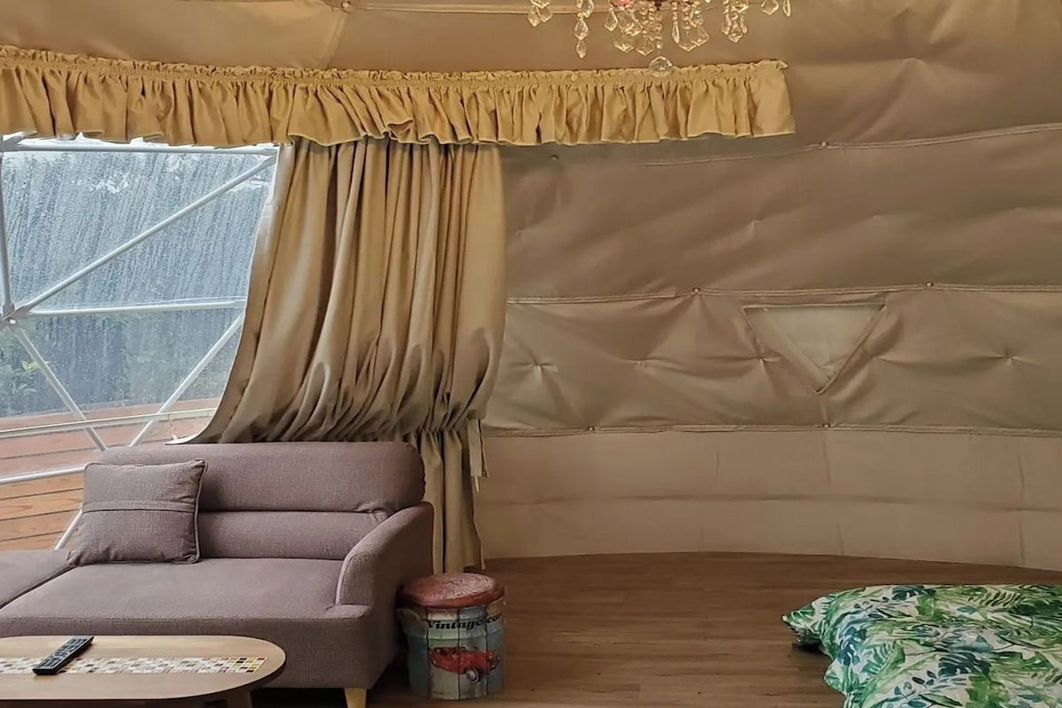 Een gezellige kamer met een bekleedde bank, een klein rond tafeltje en een raam met gordijnen.