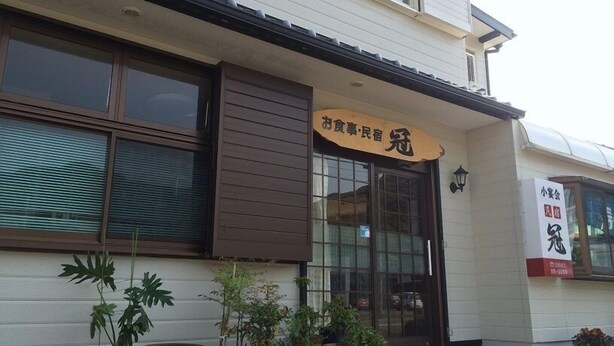 A building with a sign that reads "お食事・民宿" and another sign with "小倉会" and a phone number. There are potted plants in front. - Minshuku Kan (Tosashimizu)