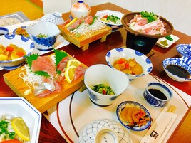 Variedad de platos que incluyen sashimi, vegetales y sopa, dispuestos sobre una mesa de madera.