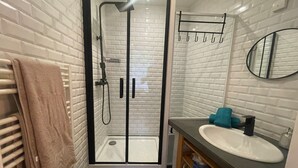 Une salle de bain moderne avec une douche à parois de verre, des murs recouverts de carreaux blancs, un lavabo blanc et un porte-serviettes.