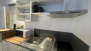 Une cuisine compacte équipée d’un four à micro-ondes, d’un évier et d’une hotte en acier inoxydable.