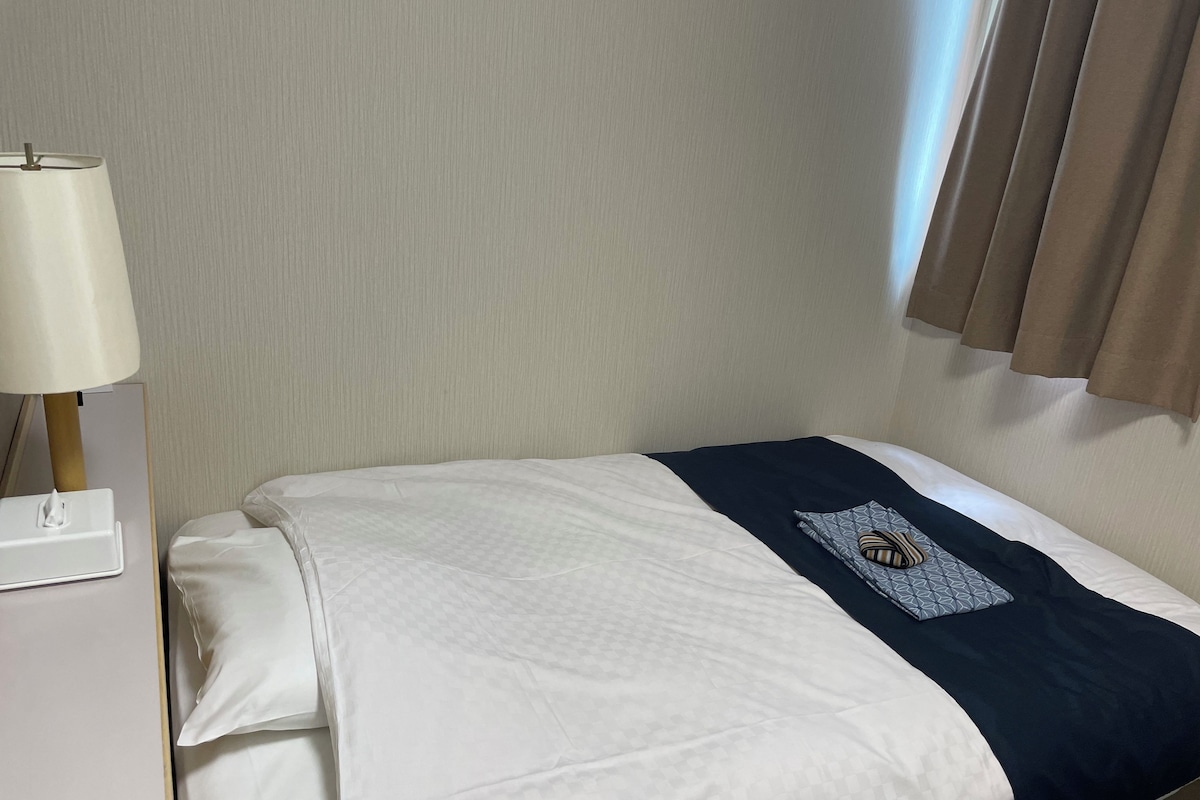 Una cama bien tendida con una colcha blanca y azul marino, una almohada blanca y una mesita de noche con una lámpara.