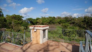A small, enclosed outdoor area with a metal railing, a concrete floor, and a beige structure with a window. - Izumibaru House (Nakijin)