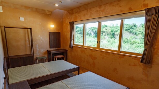 A traditional Japanese room with tatami mats, a wooden desk, a chair, and a window with curtains. - Izumibaru House (Nakijin)
