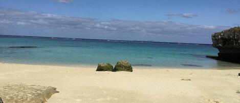 Una playa con agua turquesa cristalina, una orilla arenosa y una gran formación rocosa.
