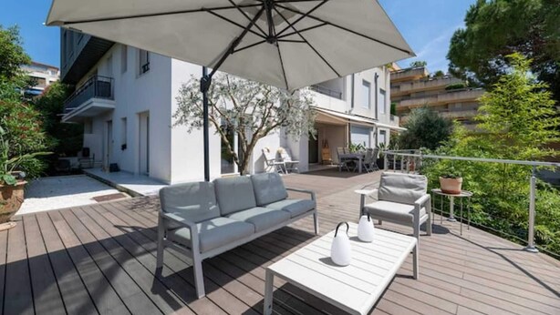 Une terrasse extérieure avec un canapé, des chaises et une table, le tout installé sous un grand parasol.